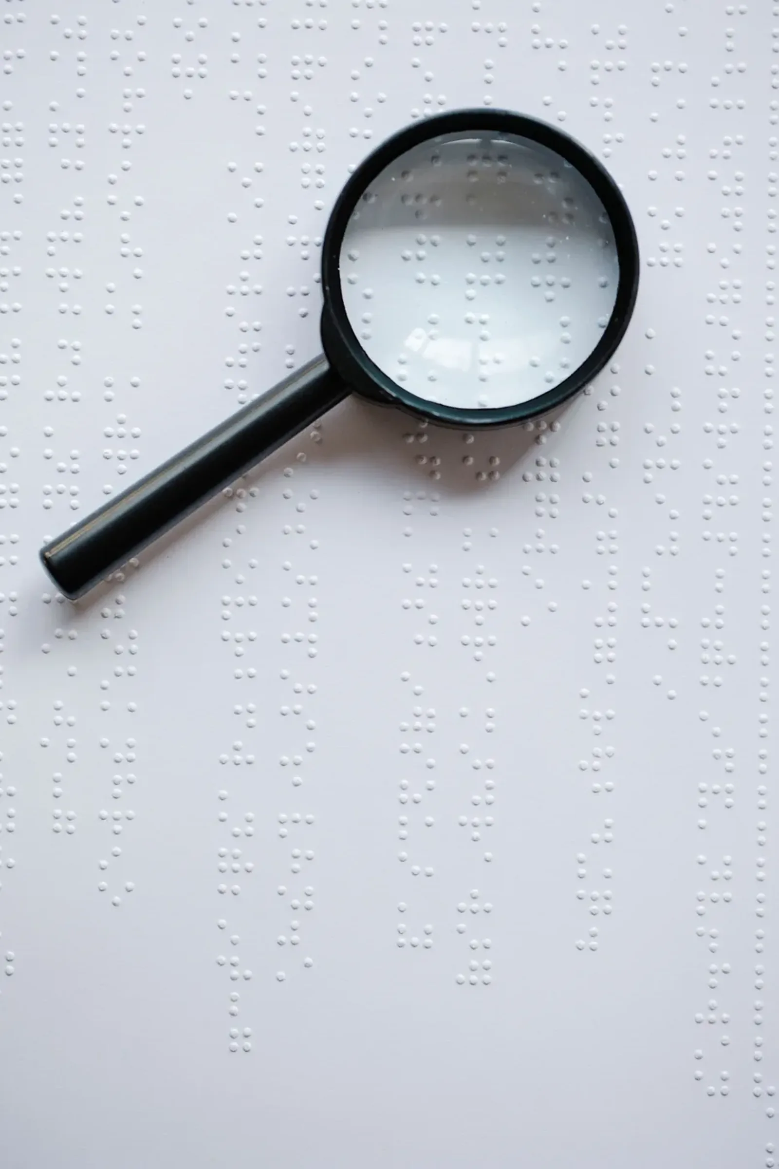 A magnifying glass resting on a page of braille