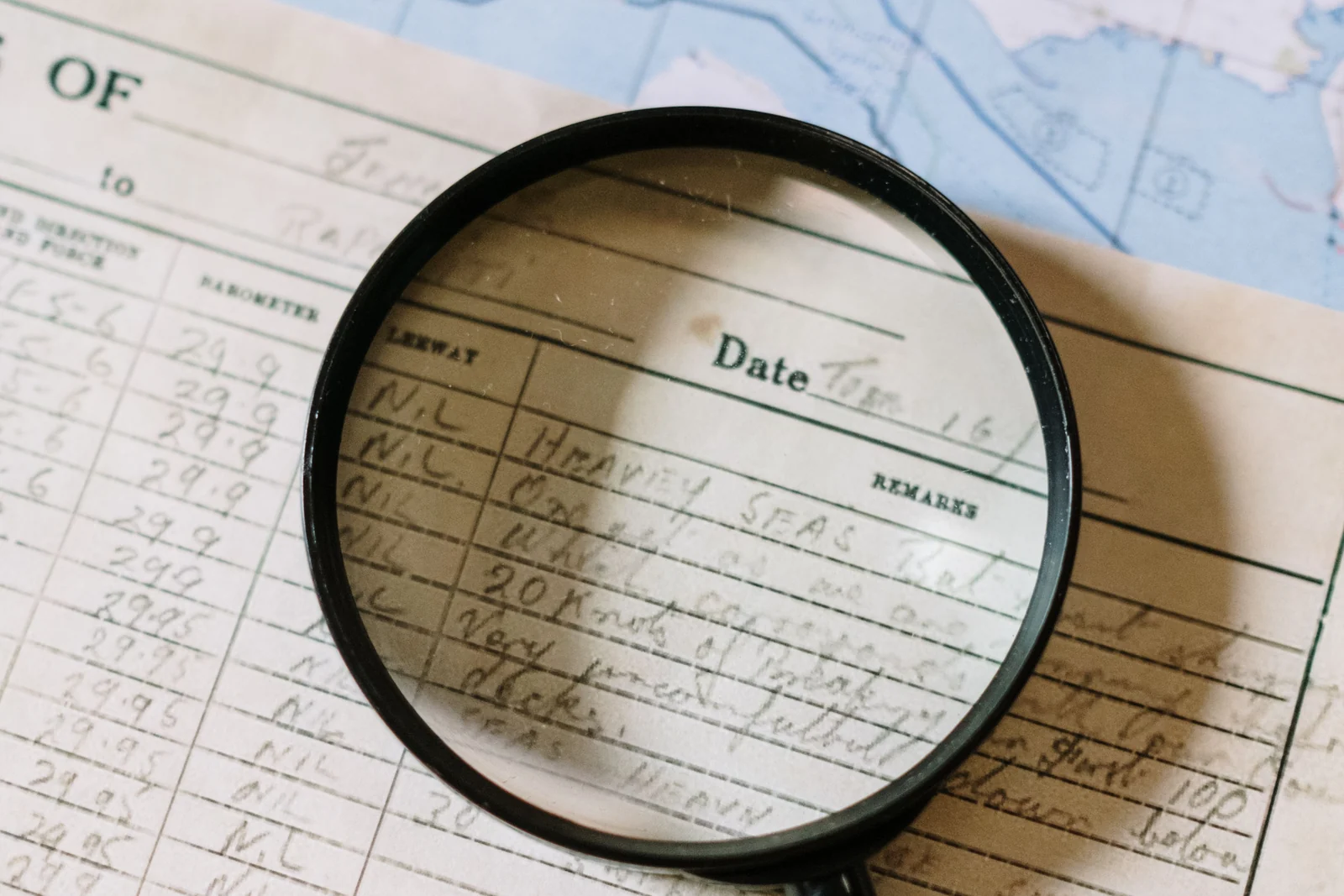 A magnifying glass over a handwritten ship logbook laid across nautical charts
