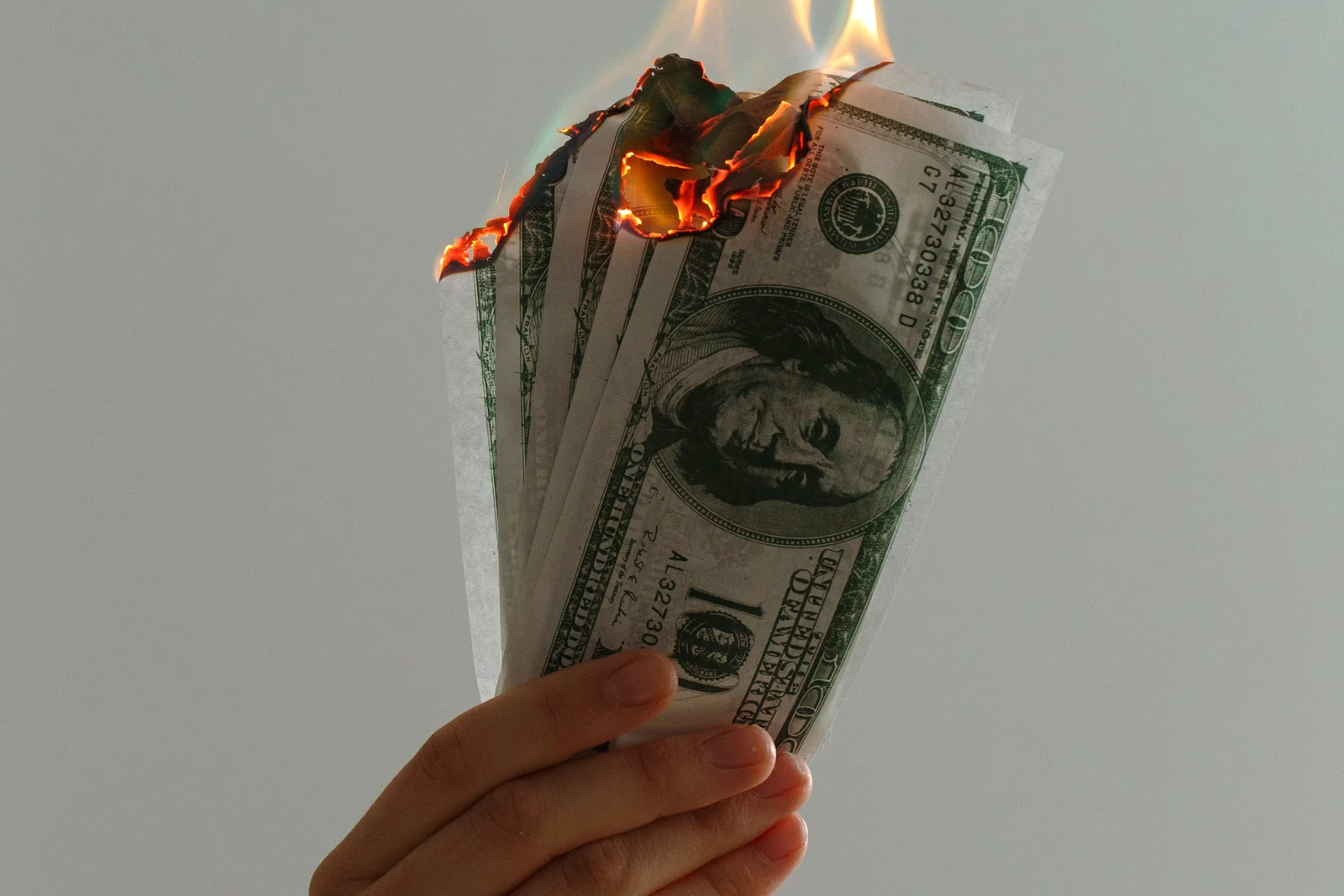 A hand holding hundred dollar bills burning at the edges