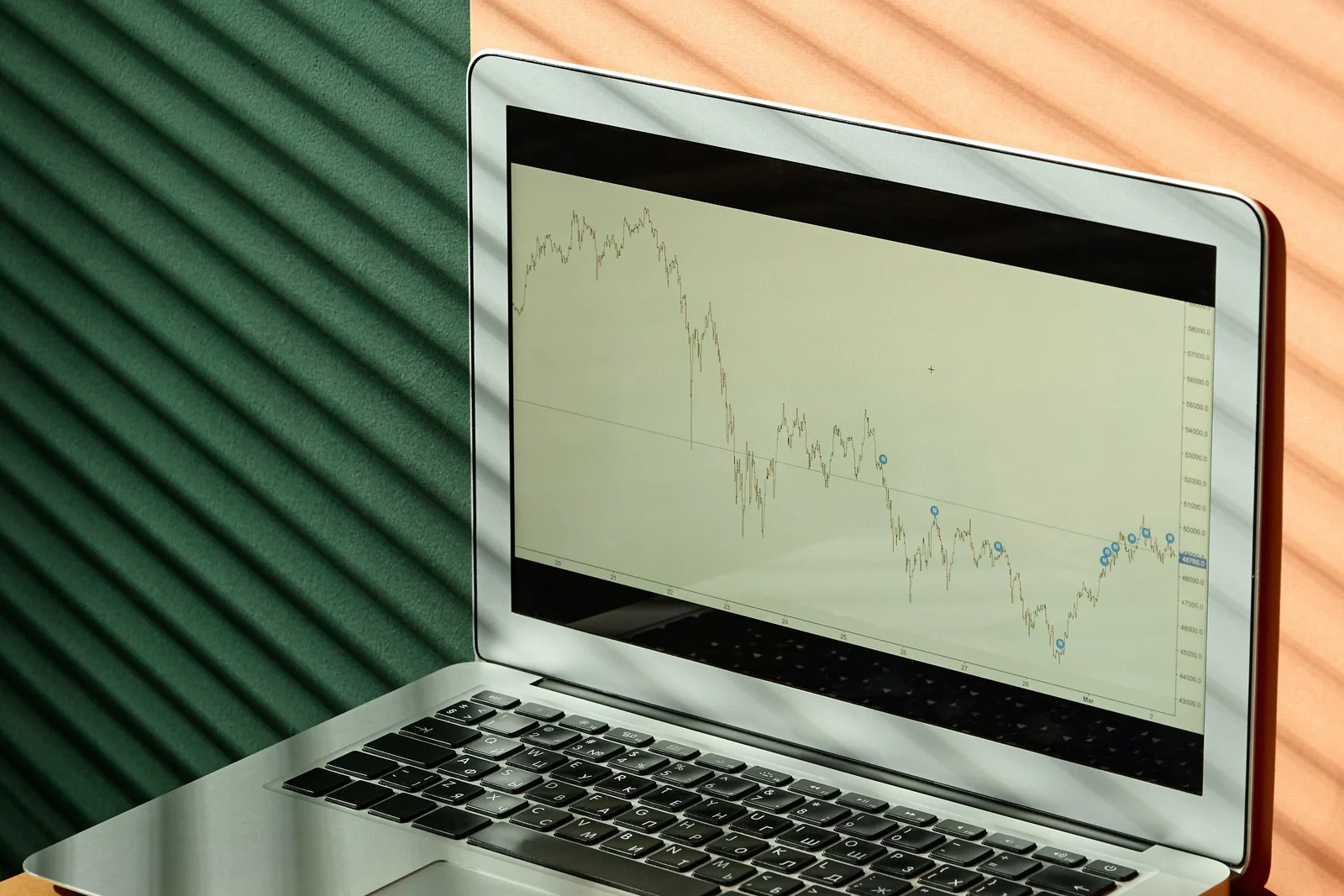 An open laptop showing a financial candlestick chart, on a desk with printed finance reports