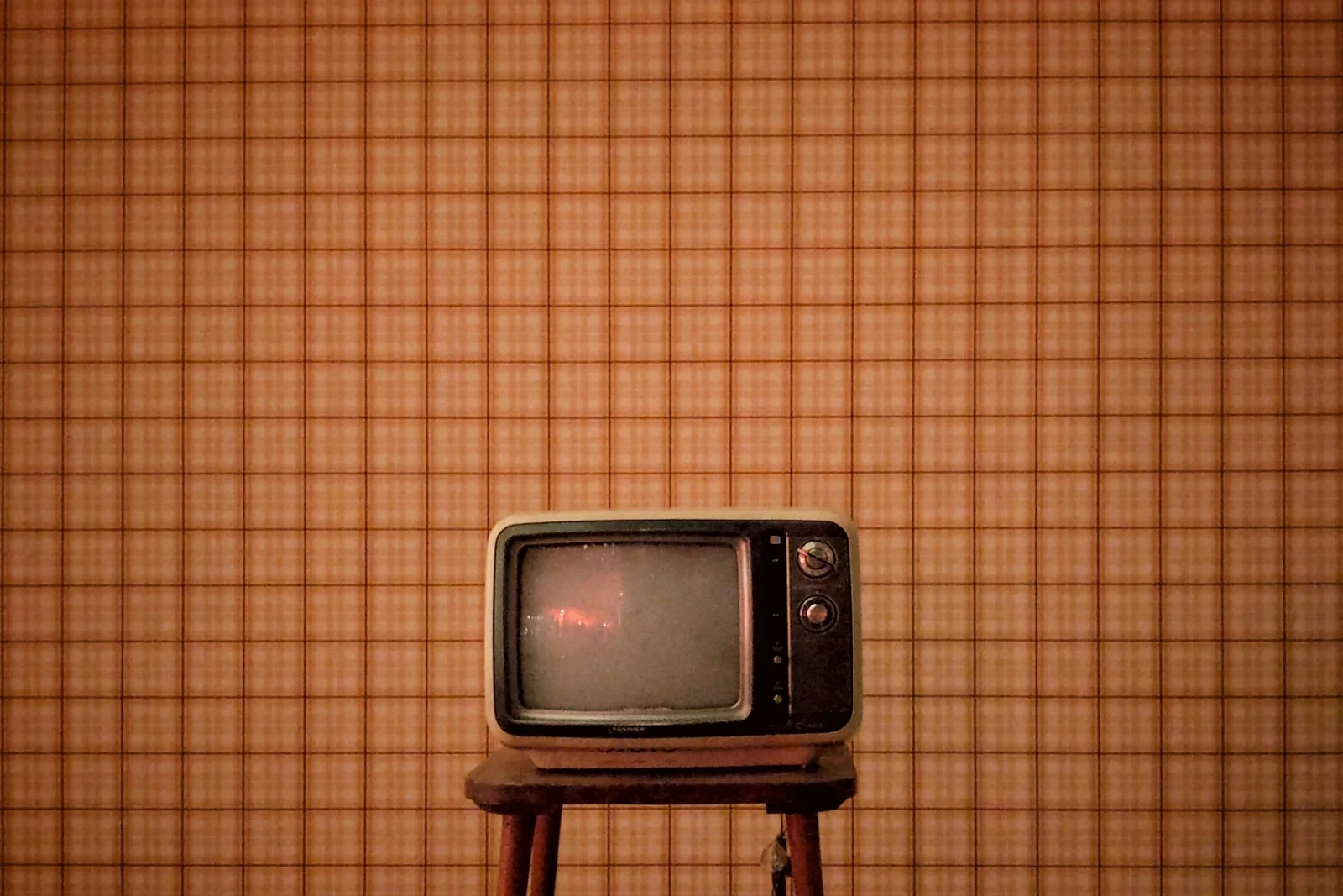 A vintage television on a wooden stool against plaid wallpaper