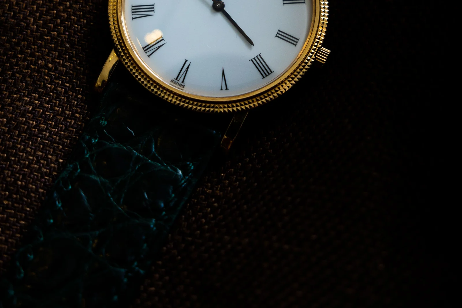 A close-up of a gold wristwatch face in warm low light, hands mid-sweep