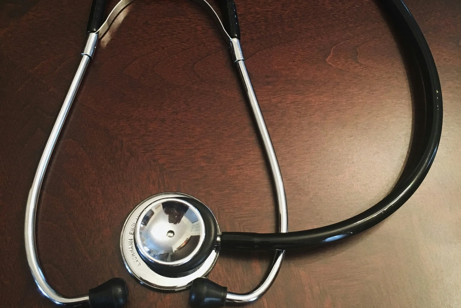 A stethoscope and a white pill on a dark wooden table