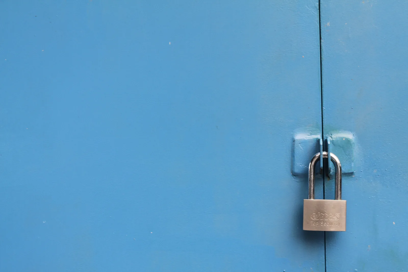A steel padlock securing a pair of blue metal doors