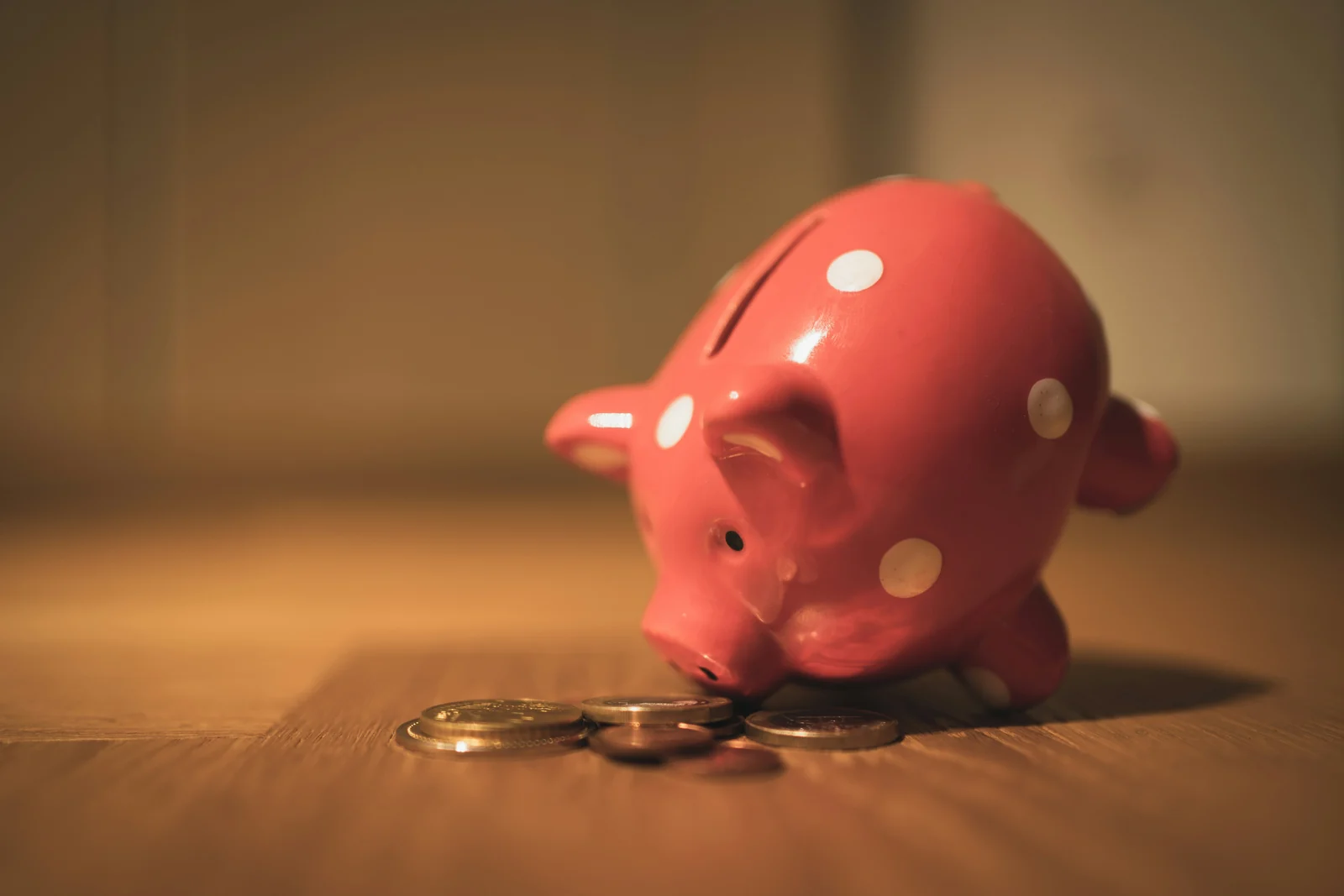 A pink polka dot piggy bank nosing a small pile of coins