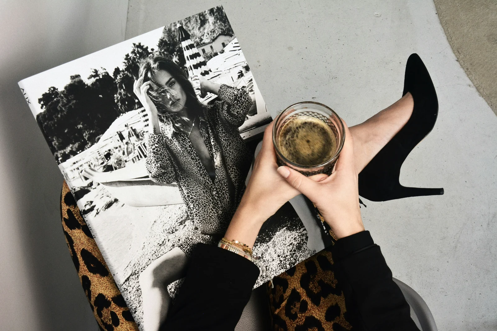 A flat lay of a fashion magazine, black heels, and a glass of coffee