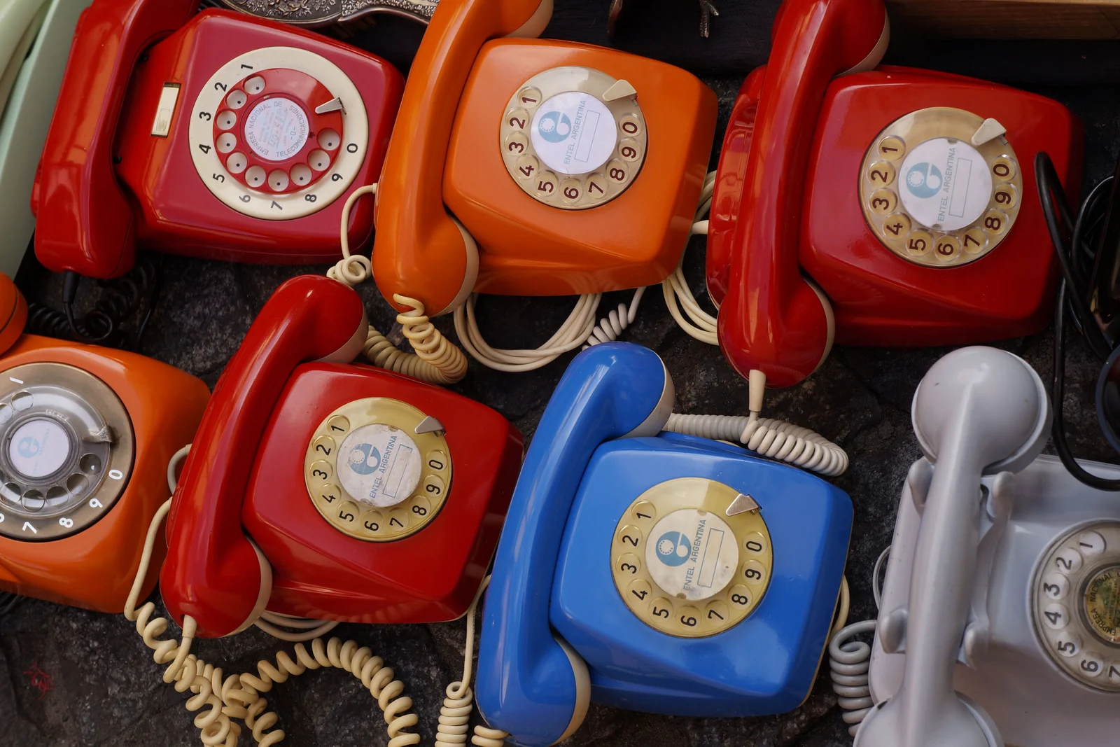 A flat-lay of vintage rotary telephones in red, orange, and blue, receivers and cords tangled
