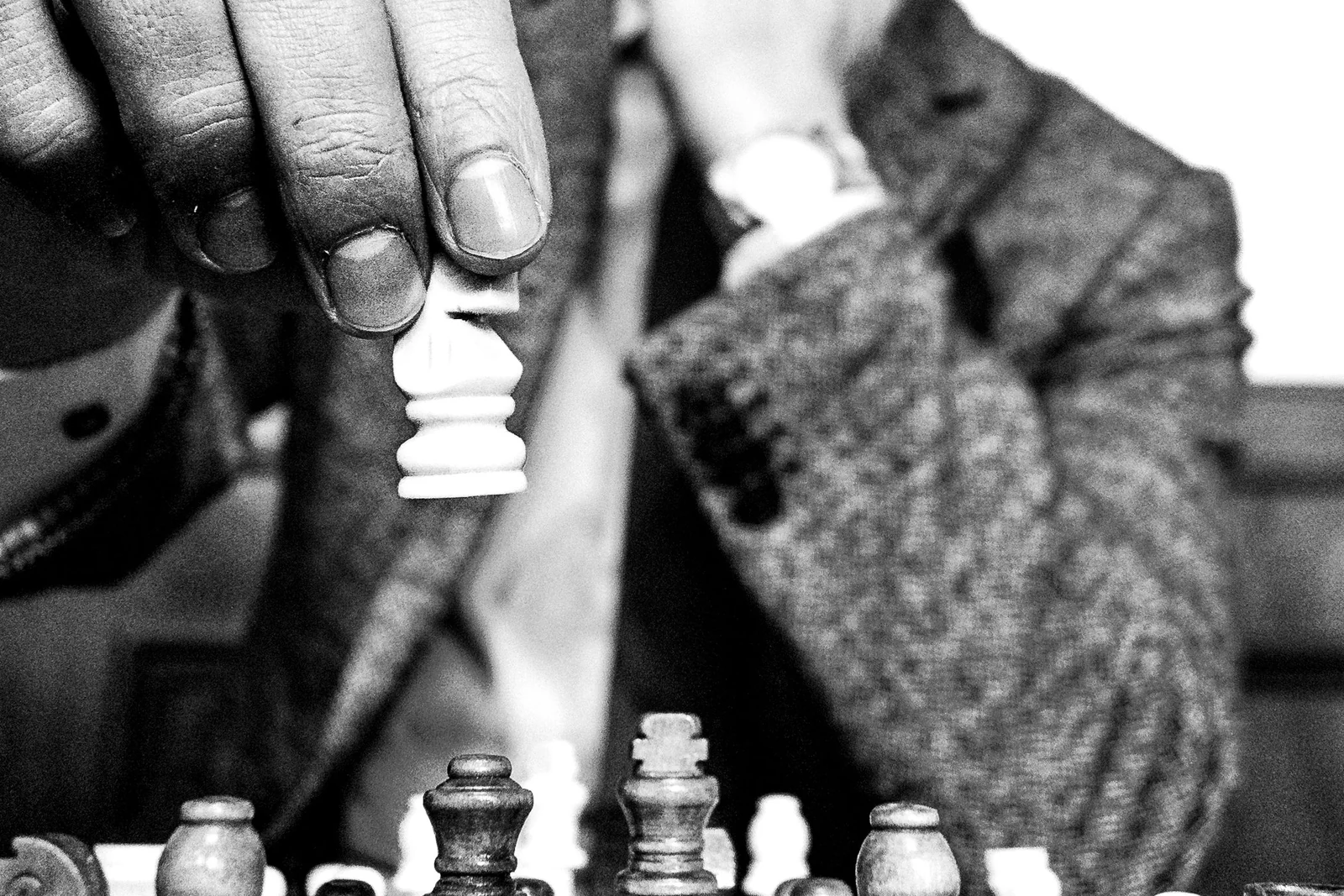 A hand lowering a chess piece into position on a crowded board, black and white