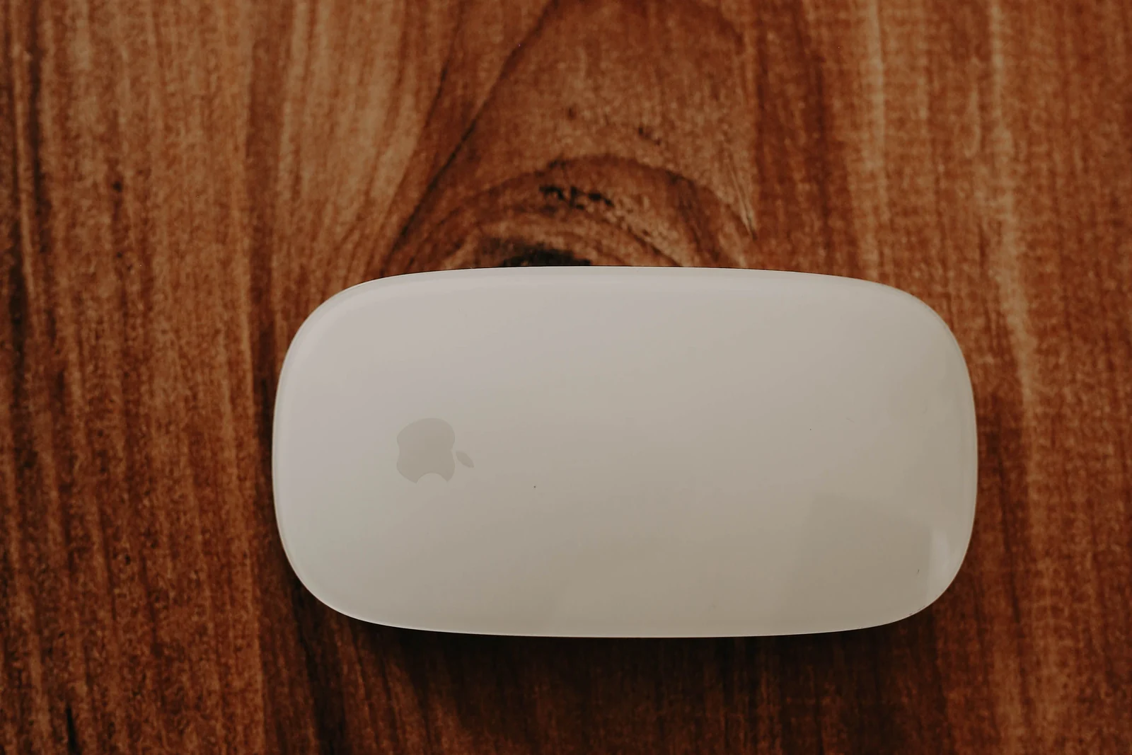 A white Apple Magic Mouse centered on a rich walnut wood surface
