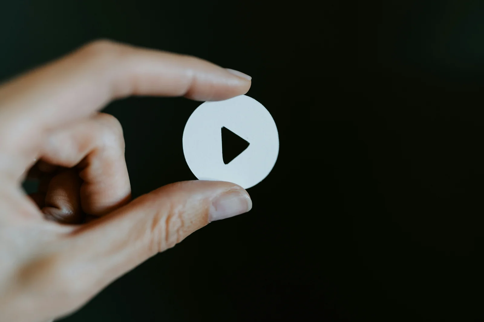 A hand holding a small white play button cutout