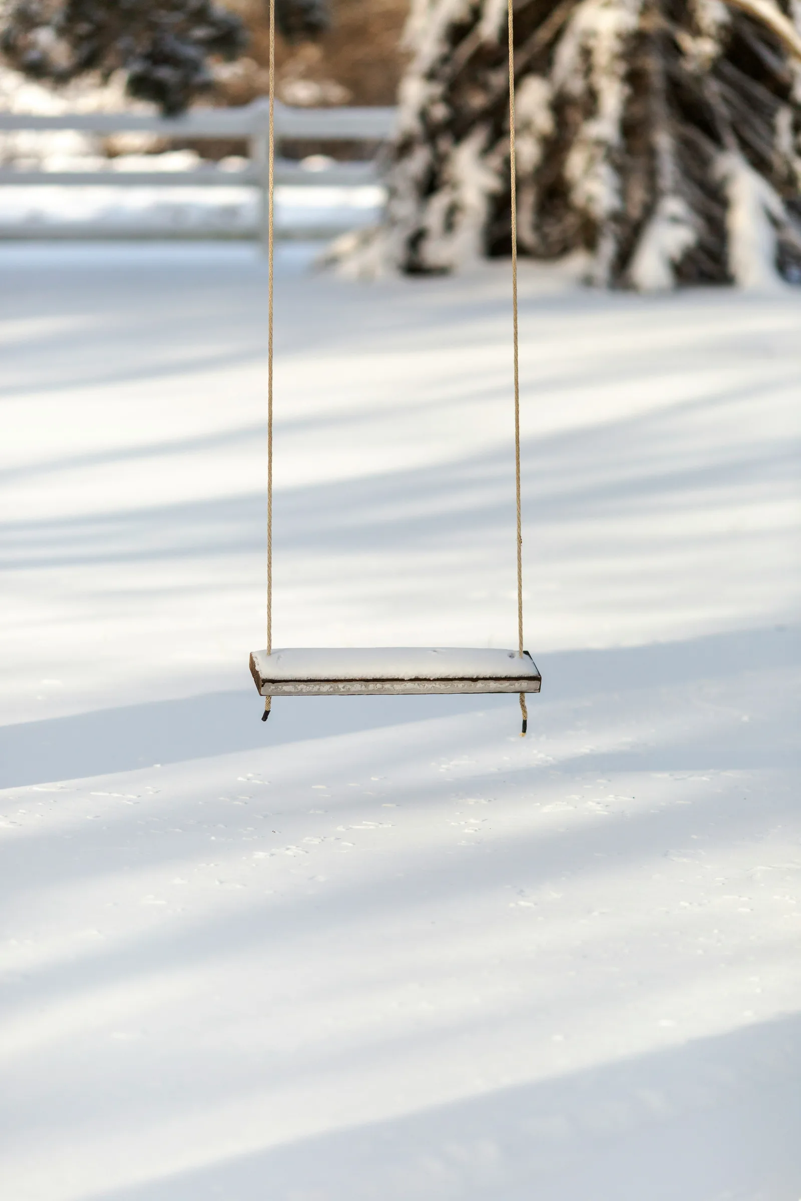 An empty wooden swing dusted with snow hanging over an untouched field
