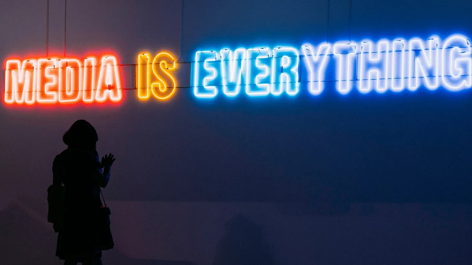 A neon sign reading MEDIA IS EVERYTHING above a silhouetted figure: digital marketing and advertising for media and technology companies
