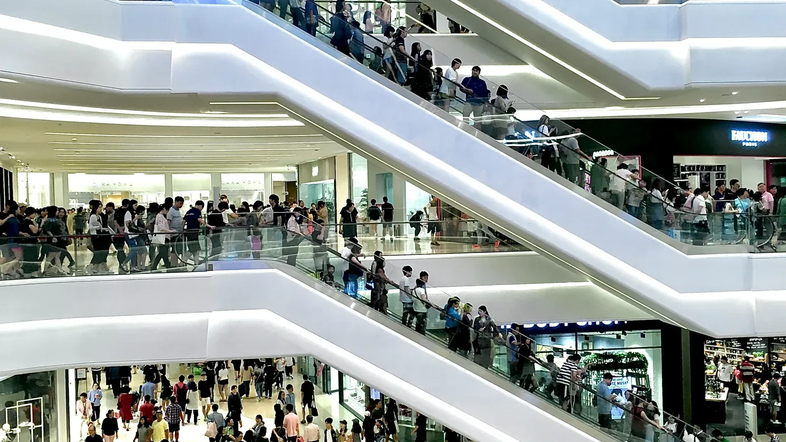 Menschen auf den Rolltreppen eines mehrstöckigen Einkaufszentrums: Digitalmarketing und Werbung für Händler und Shoppingcenter